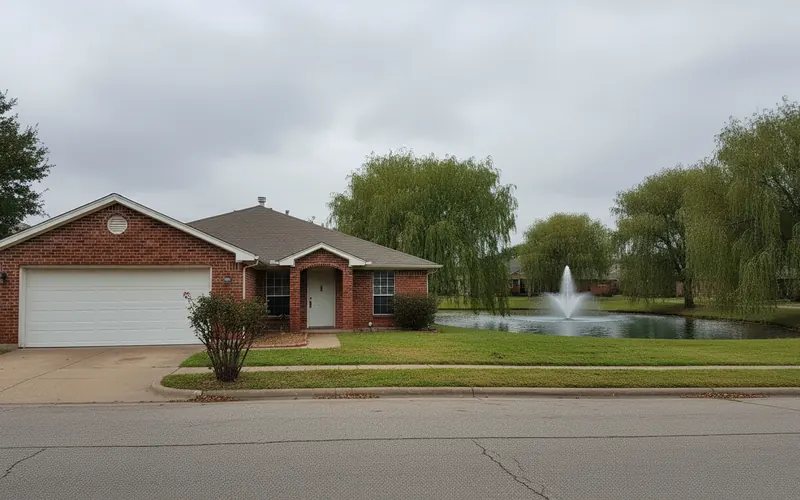 Single-story 1970s brick home with a single garage door beside a small lake in Country Place, Carrollton